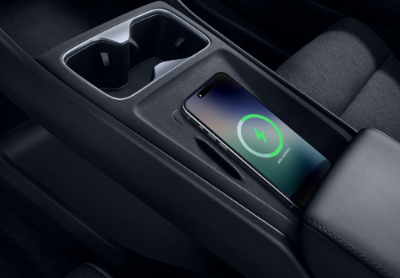 Smartphone wirelessly charging in a car's centre console next to cup holders.